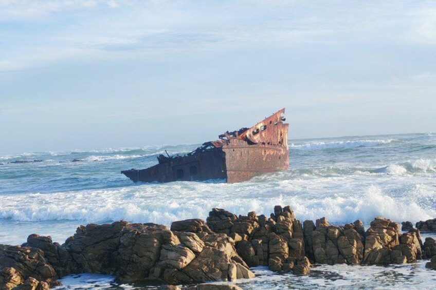 A shipwreck on a rocky shore with waves crashing against it. 2