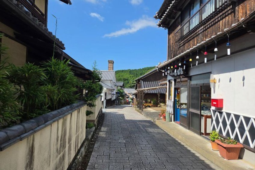 A narrow cobblestone street lined with traditional wooden buildings, a small stream, and a clear blue sky. 2