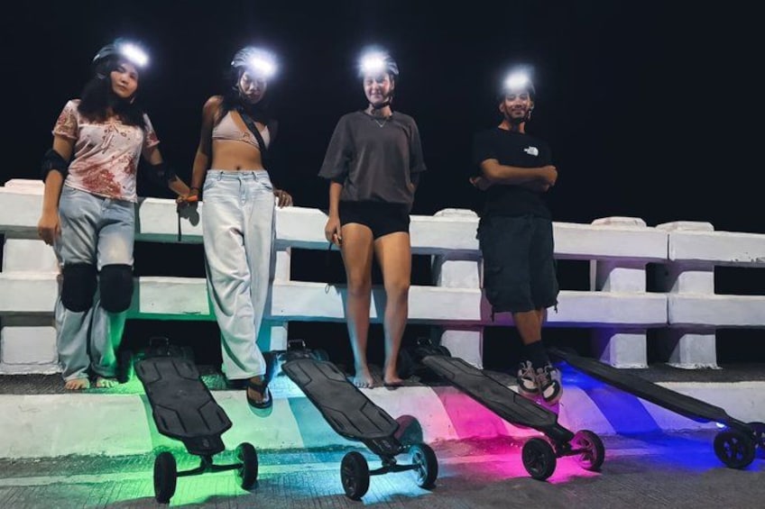 Four people standing on a rooftop with skateboards and LED lights. 1