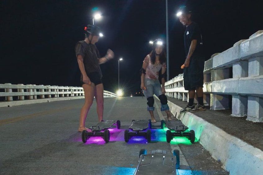 People on a bridge at night with illuminated skateboards. 3