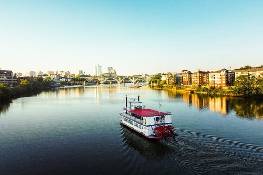 Un bateau à vapeur navigue sur une rivière paisible, avec la silhouette d’une ville et un pont en arrière-plan. 2