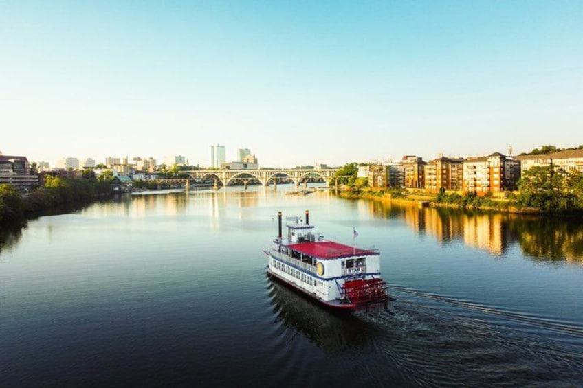 A riverboat on a calm river with a city skyline and bridge in the background. 3