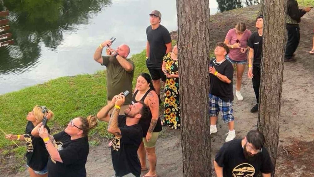 A group of people near a body of water, some holding cameras or phones, possibly taking photos or videos. 4