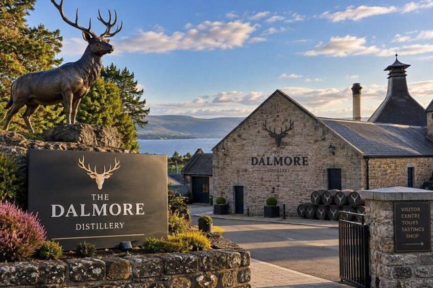 The Dalmore Distillery building, a sign with a deer head logo, and a statue of a deer. 5