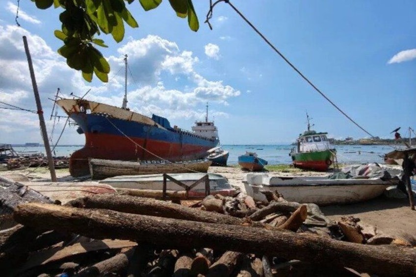 A dock with several boats, including a large blue and red ship, and smaller boats in the background. 1
