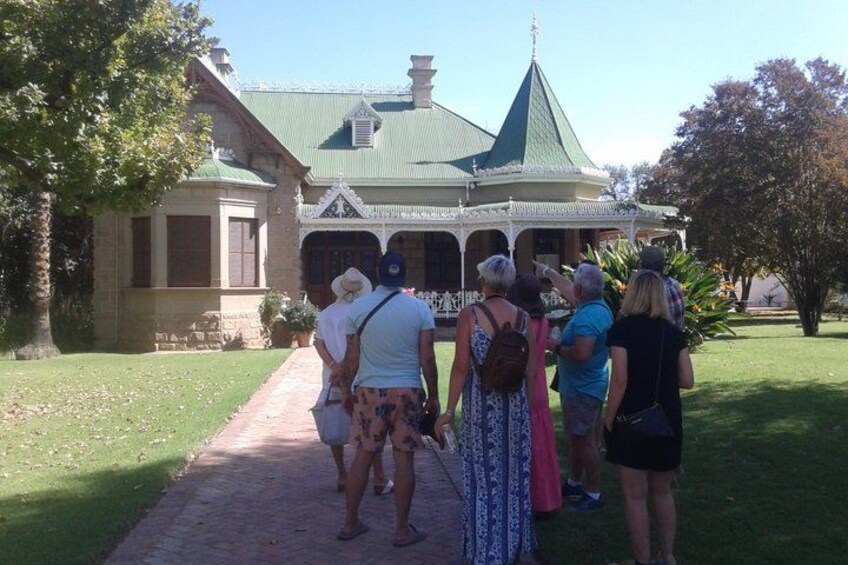 A group of people standing on a pathway in front of a building with a green roof and white trim. 3