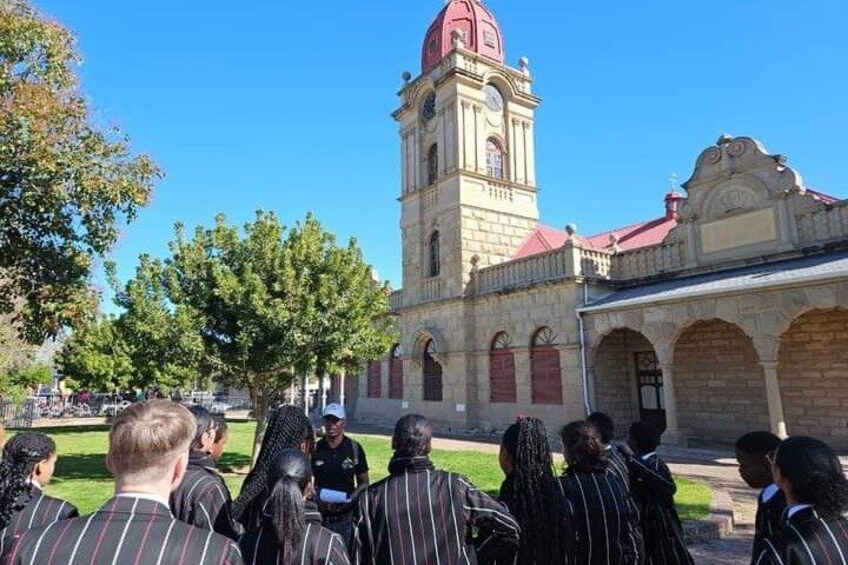 A group of people in front of a historic building with a clock tower and arched windows. 5