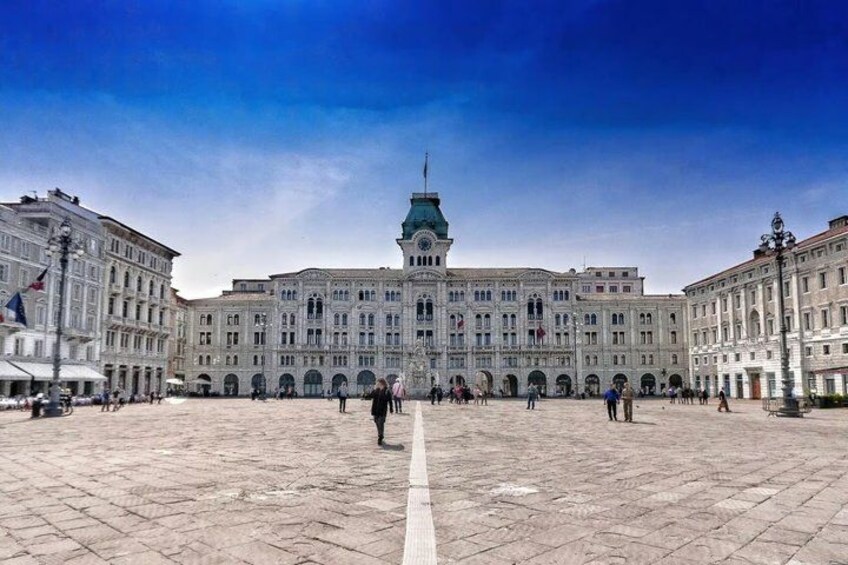 A large historic building with a central tower, surrounded by a paved square with people walking. 5
