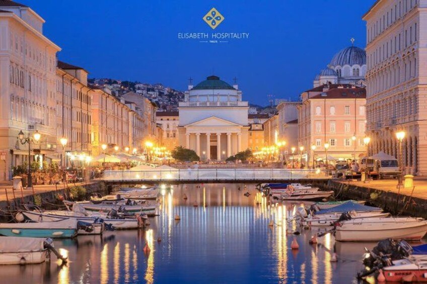 A waterfront with boats docked, a prominent building with columns, and a dome structure in the background. 1