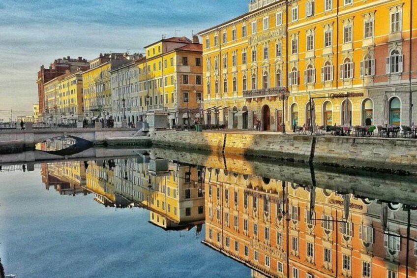 A canal with buildings reflecting on the water, a bridge, and a clear sky. 3