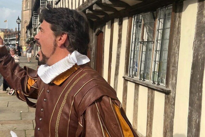 A person in historical costume standing in front of a building with a white and brown facade. 2