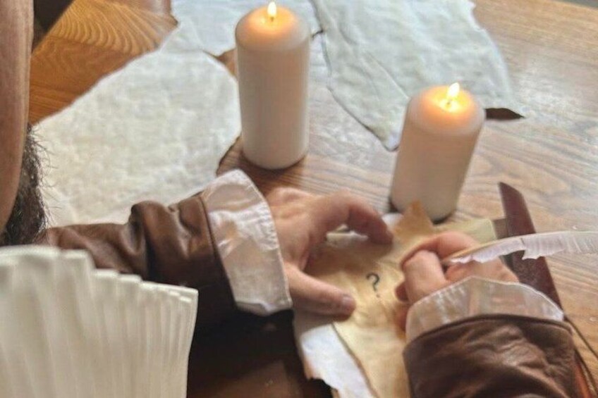 A person handling a leather item with a feather and a candle on a wooden surface. 3