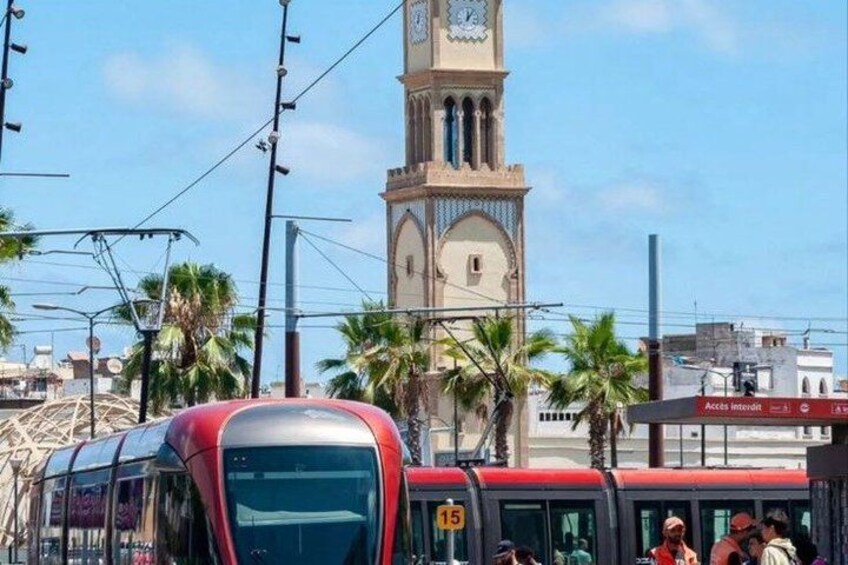 A red tram with passengers, a clock tower, and palm trees. 1