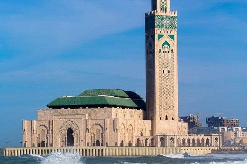 A large mosque with a tall minaret, a green roof, and a coastal backdrop. 5