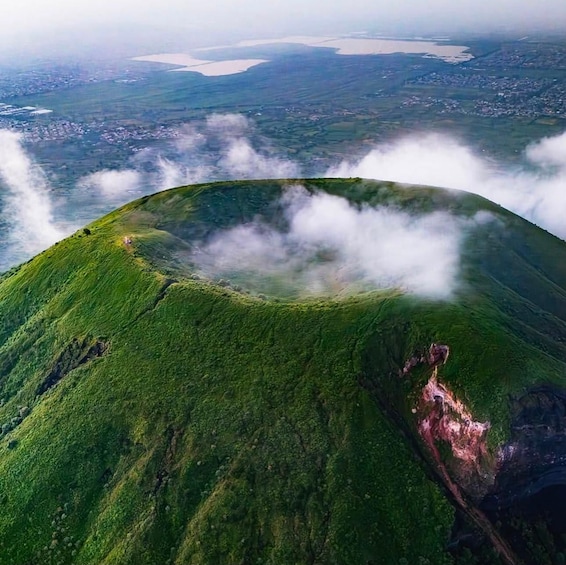 A lush green mountain with a crater surrounded by clouds. 1