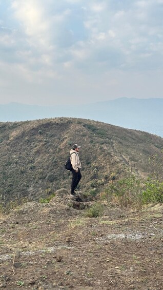 A person hiking on a dry, rocky hillside with sparse vegetation under a cloudy sky. 4
