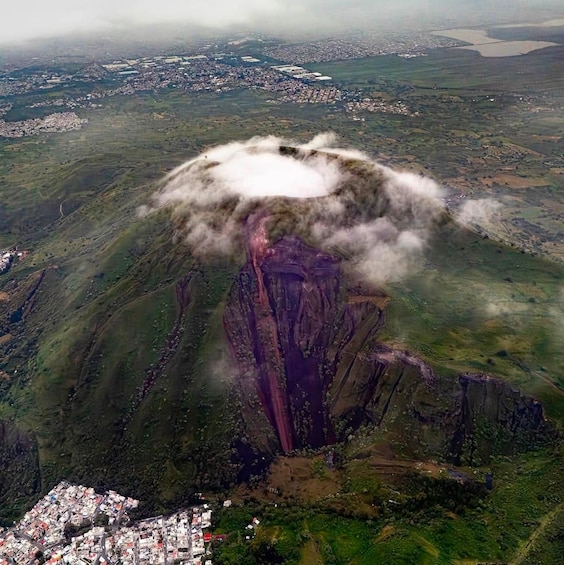 An aerial view of a mountainous landscape with a prominent peak, a valley with scattered buildings, and a distant body of water. 2