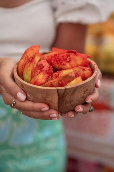 A person holding a wooden bowl filled with sliced peaches. 2