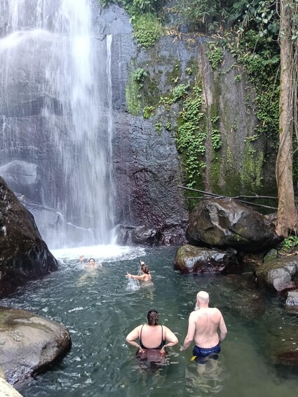 A waterfall, rocky terrain, and people swimming in a natural pool. 4