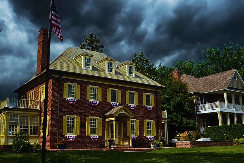 A large brick building with yellow shutters, decorated with American flags and a wreath, under a stormy sky. 3