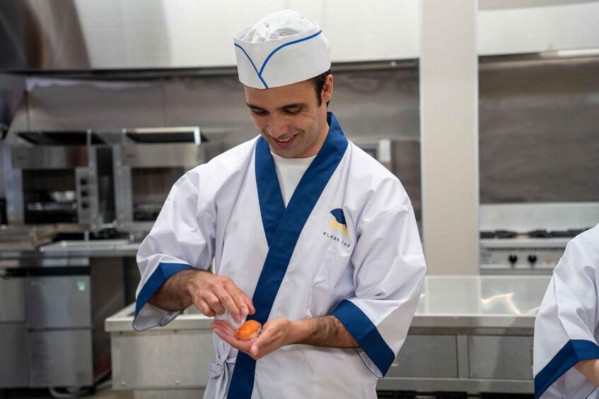 A chef in a white uniform with blue trim, preparing a piece of sushi. 5