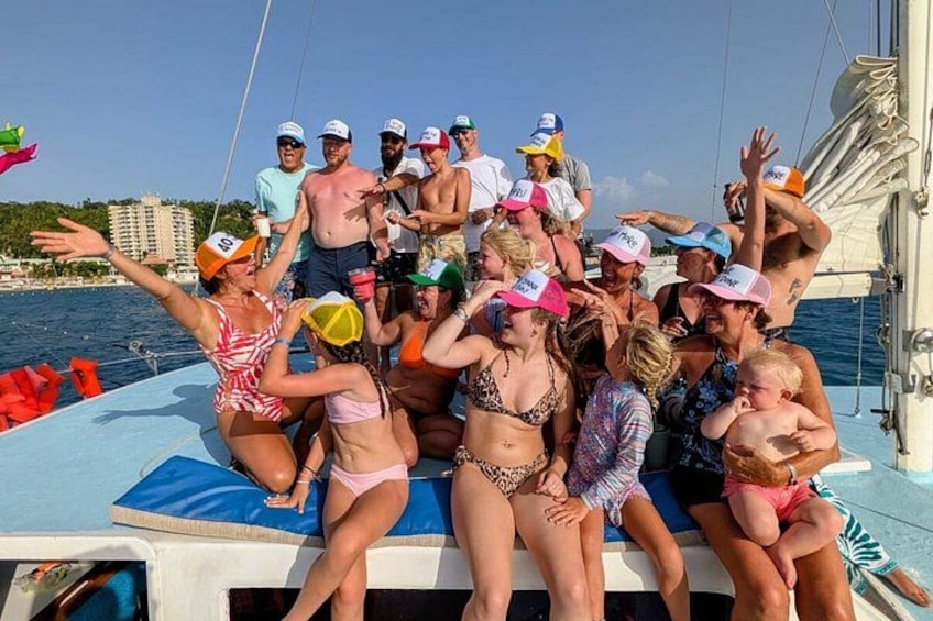 A group of people on a boat, some wearing hats, with a body of water and buildings in the background. 2