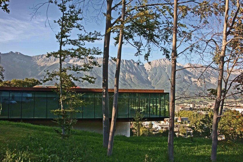 A modern building with glass walls, surrounded by trees and mountains in the background. 1