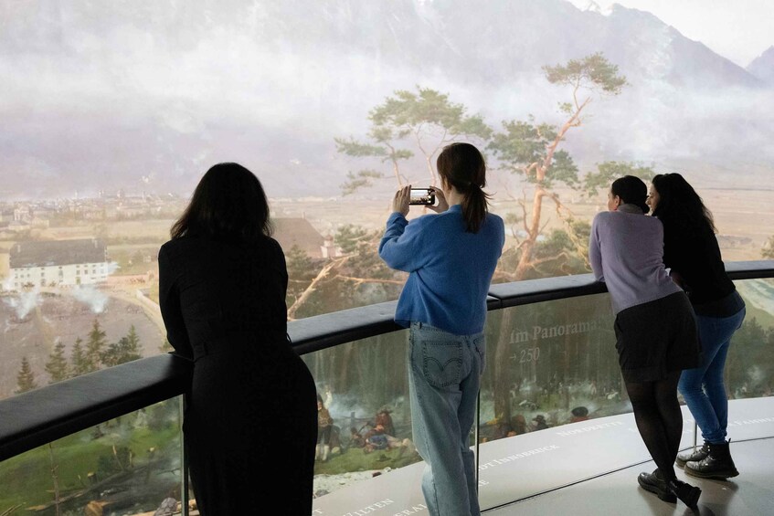 A group of people taking photos at a scenic overlook with a view of a town and mountains in the distance. 5