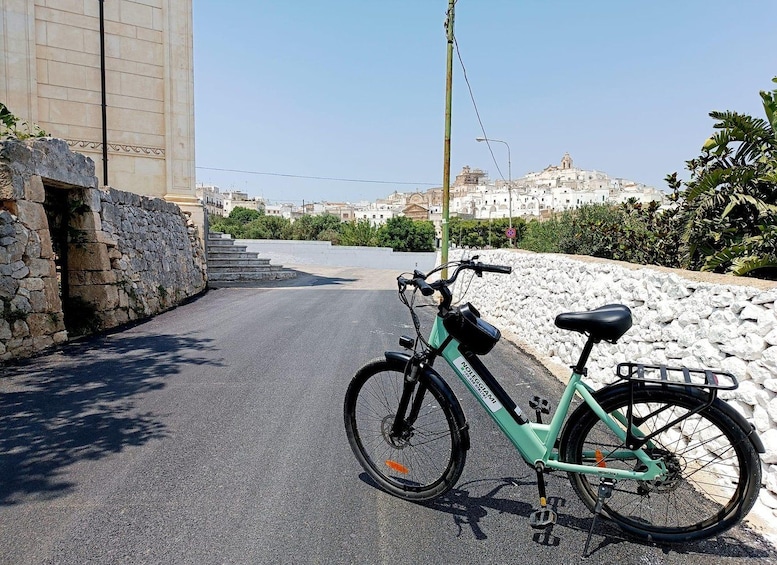 A teal bicycle parked on a paved road with a stone wall on one side and a building on the other. 3