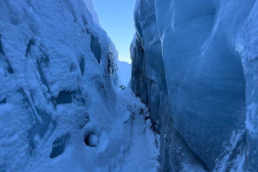 A narrow, snow-covered ice passage with a visible crevasse. 3