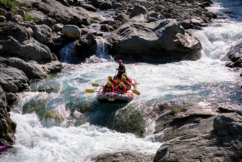 A group of people in a raft navigating a river with rapids, surrounded by large rocks and a waterfall. 1