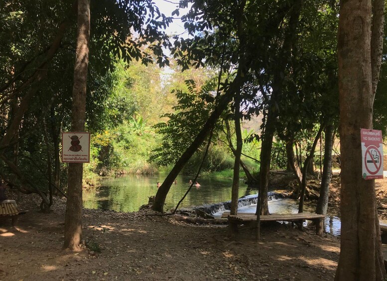 A forested area with a river, picnic tables, and signs prohibiting smoking and stone collection. 2