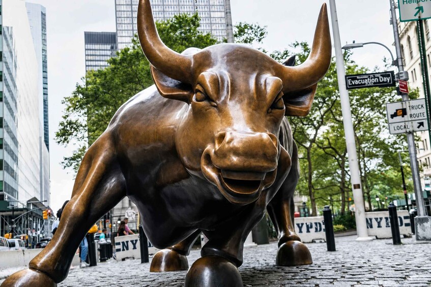 A bronze bull sculpture on a cobblestone street with buildings and a street sign in the background. 2