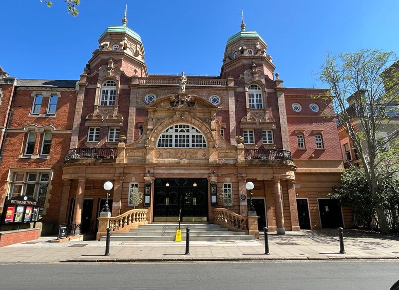 A historic theater building with ornate architecture, including a central dome and two smaller domes on either side. 5