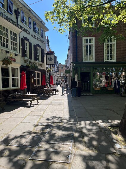A cobblestone street lined with historic buildings, outdoor seating at cafes, and a clear blue sky. 2