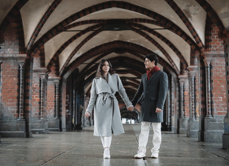A couple holding hands in a covered pedestrian walkway with brick arches and columns. 4