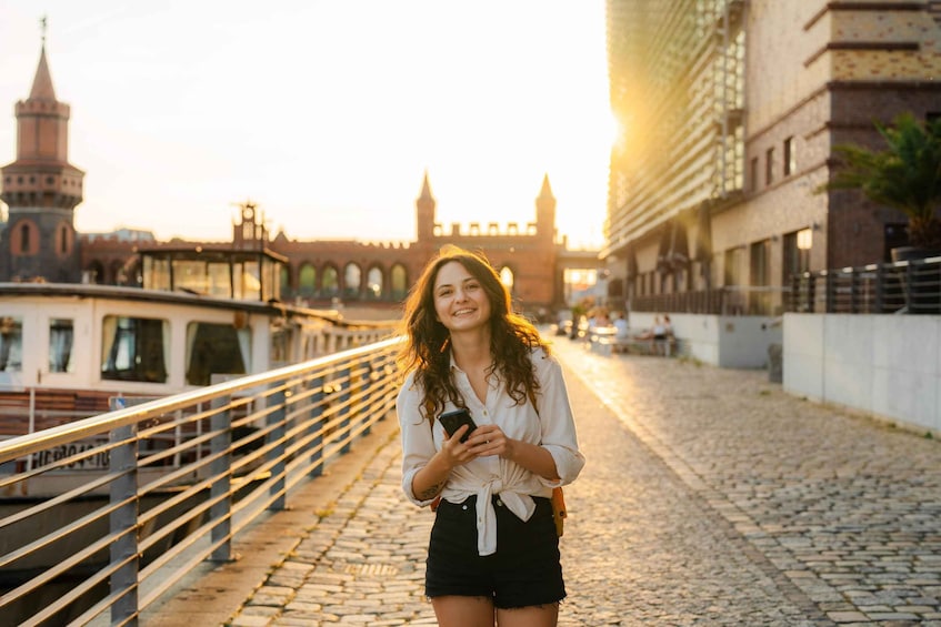 A person standing on a cobblestone street with a historic building and a tower in the background. 1