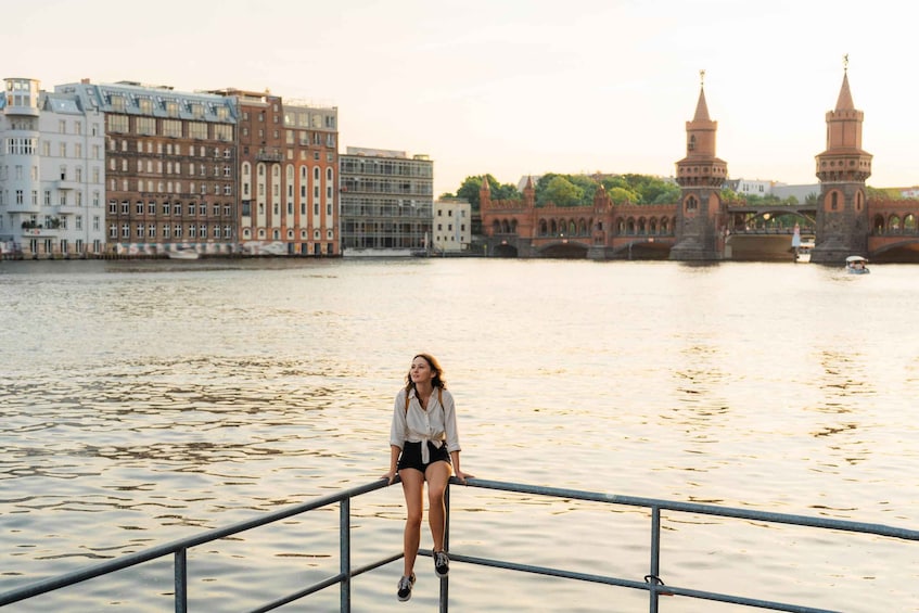 A person sitting on a railing by a river with buildings and a tower in the background. 5