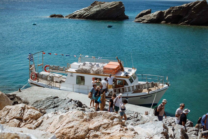 A boat docked at a rocky shore with people boarding and disembarking. 2