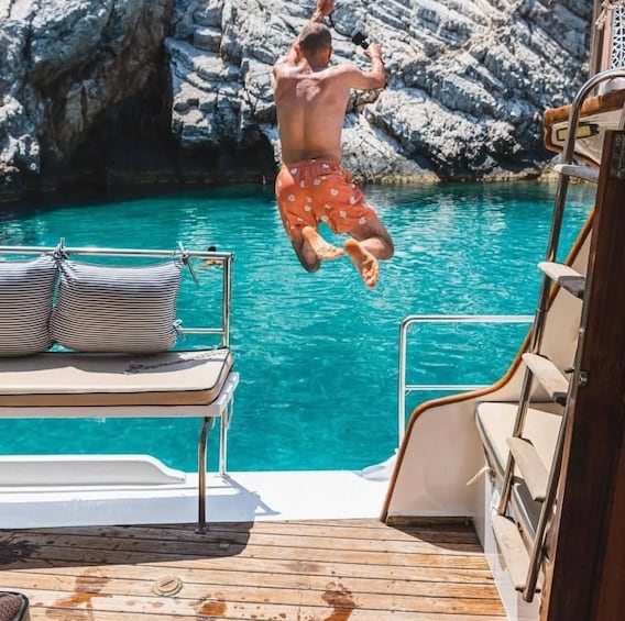 A person jumping off a boat into a turquoise sea with rocky cliffs in the background. 1