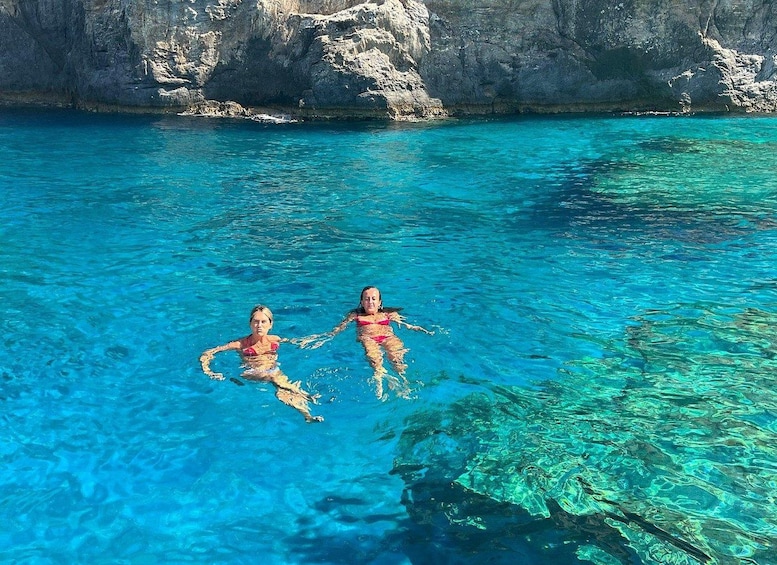 Two people swimming in clear blue water with rocky cliffs in the background. 3