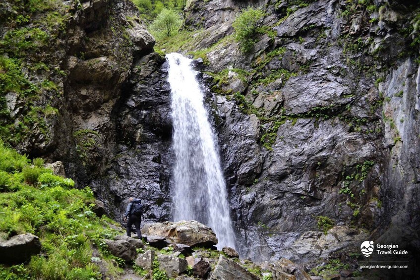 A waterfall cascading down a rocky cliff surrounded by lush greenery. 2