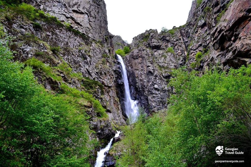A waterfall cascading down a rocky cliff surrounded by lush greenery. 3