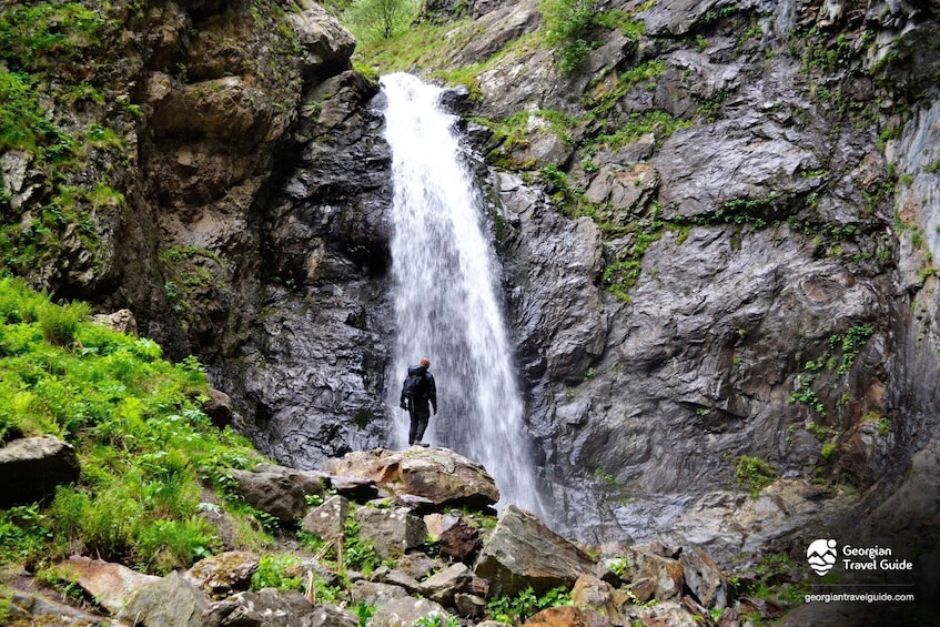 A waterfall in a rocky gorge with a person standing on a rock. 5