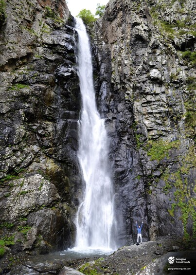A waterfall cascading down a rocky cliff with a person standing at the base. 1