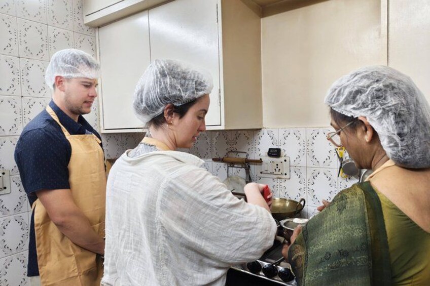 Three people in a kitchen, wearing hairnets and aprons, cooking together. 1