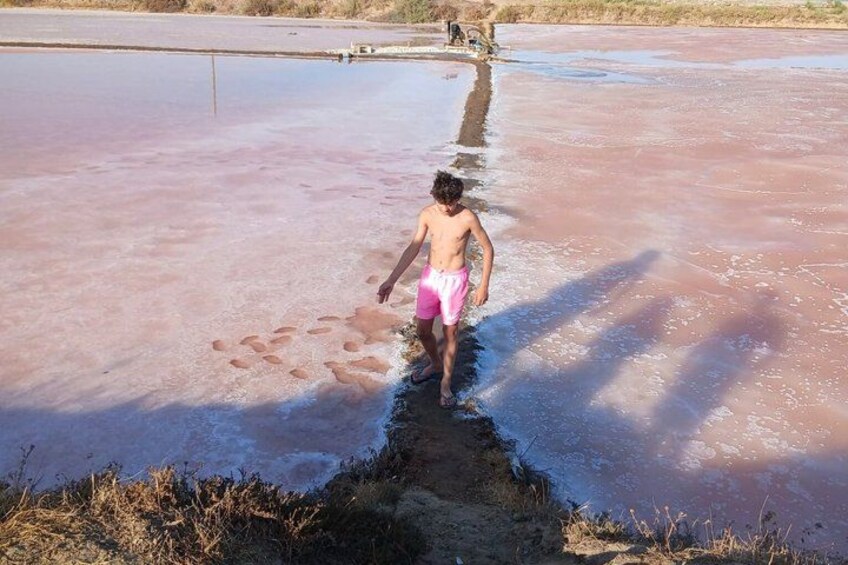 A person walking through a shallow, muddy water body with a reddish hue. 4