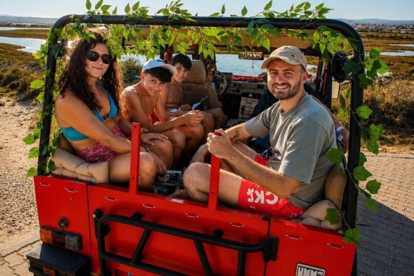 A red vehicle with passengers, surrounded by greenery and a body of water in the background. 1