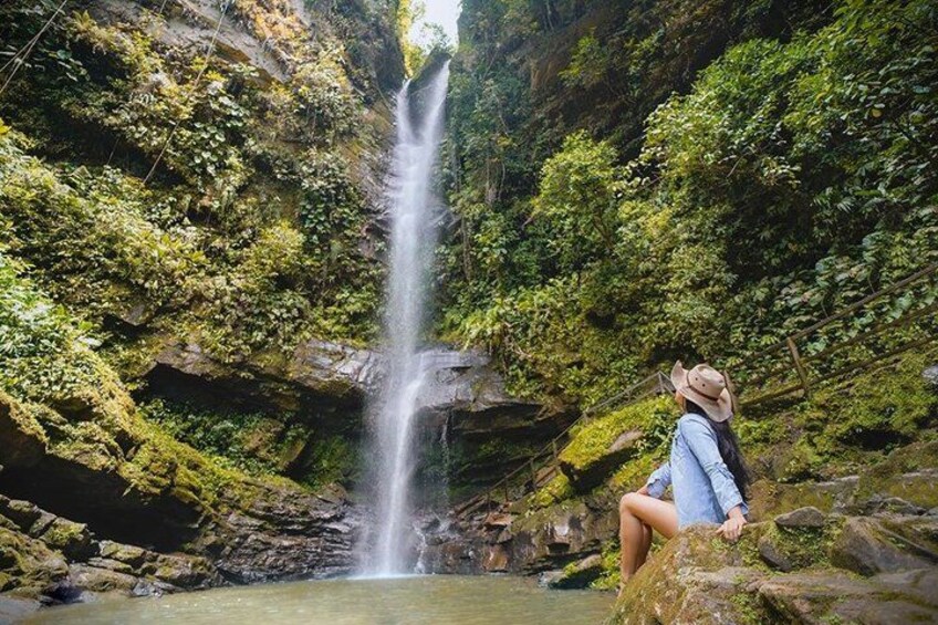 A waterfall in a forested area with a person sitting on a rock. 2