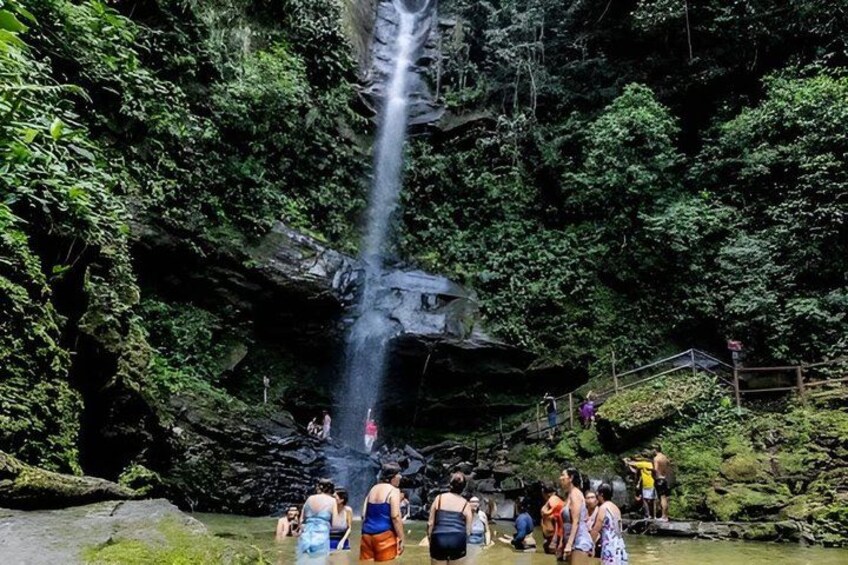 A waterfall in a forested area with people standing around the base. 3